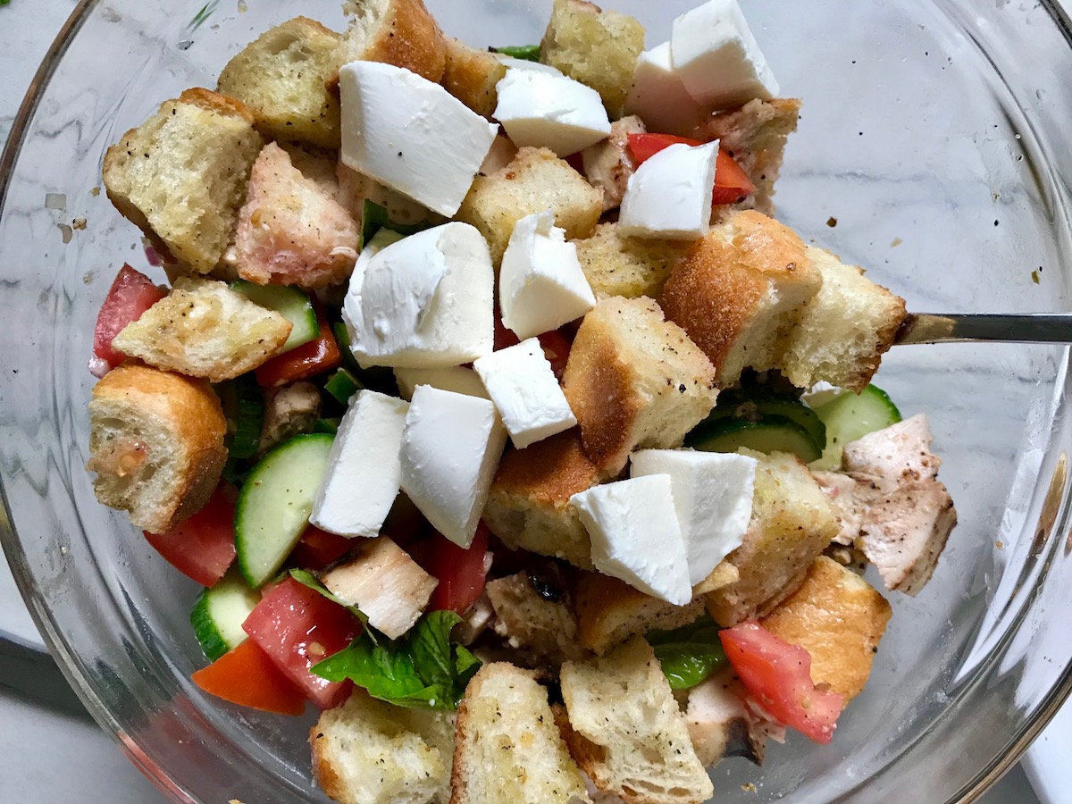 Toasted bread cubes, chicken, tomatoes, cucumber, basil, and mozzarella in a bowl for this Chicken Panzanella Salad Recipe. It's absolutely delicious.