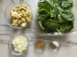 Prepped ingredients on counter for Spinach Artichoke Chicken Stuffed Pitas. From left top to right: chopped artichoke hearts, baby spinach leaves, diced onion, minced garlic, salt and pepper.