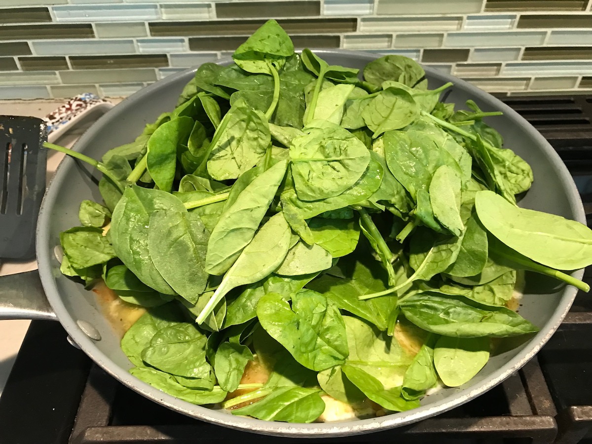Fresh Baby spinach overflowing in a pan as it starts to cook into the Spinach Artichoke Chicken filling. It will be the stuffing in the Grilled Chicken Pita recipe.