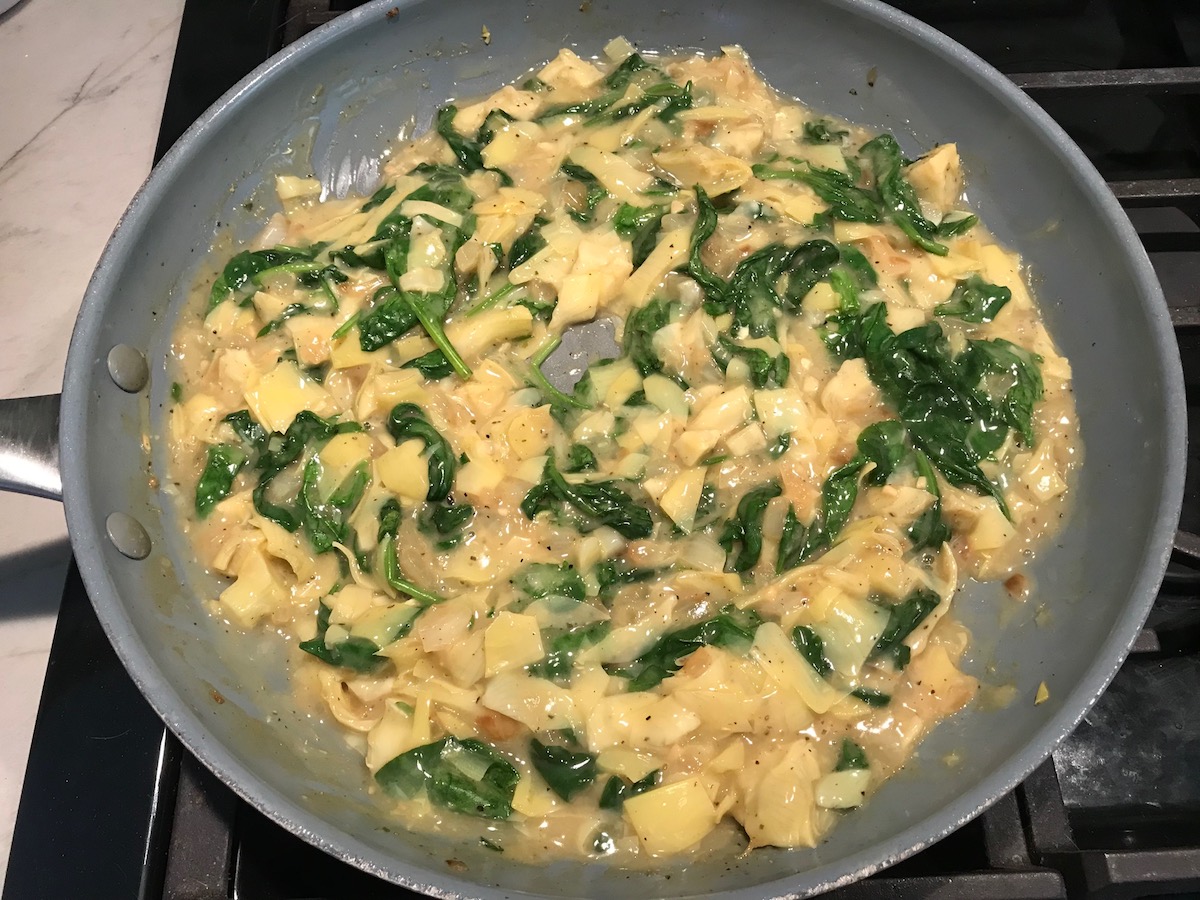 Spinach Artichoke Chicken filling in a large pan on stove for stuffing into pitas and then grilling.