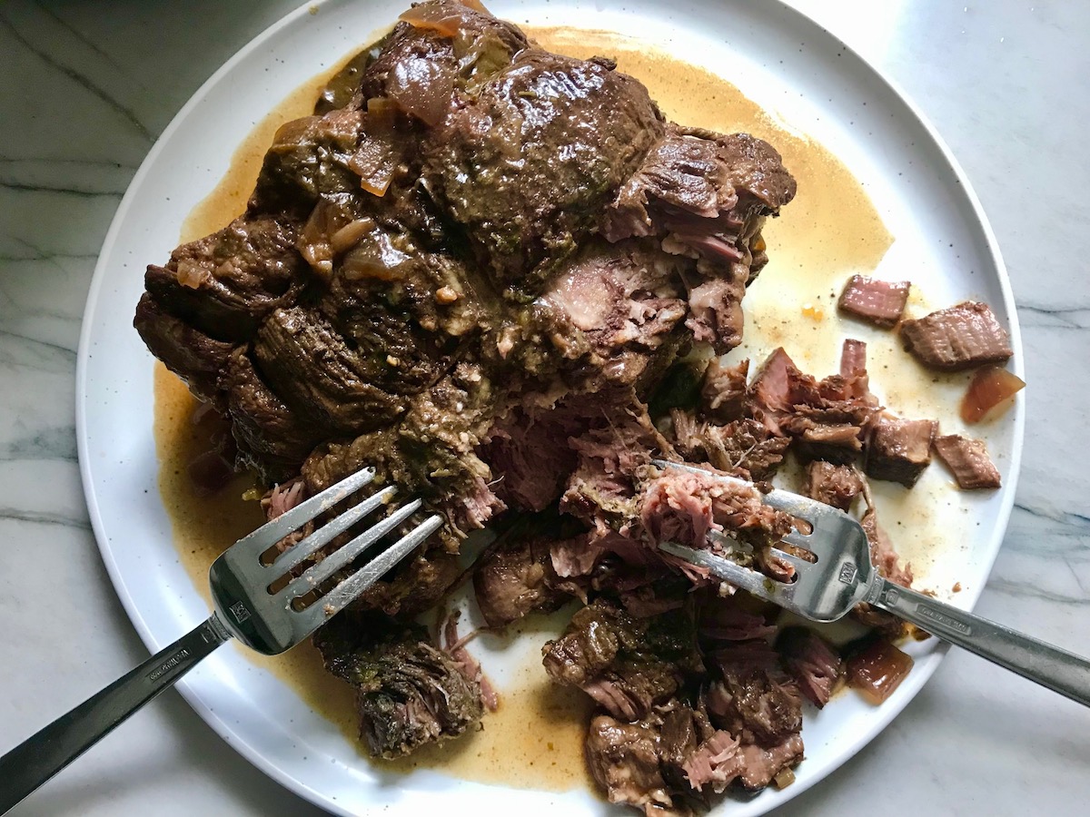 Two forks shredding beef chuck roast on a plate for Birria Tacos. This Birria Tacos Recipe in the Slow Cooker has shredded beef and Oaxaca cheese melted together in corn tortillas in a pan.