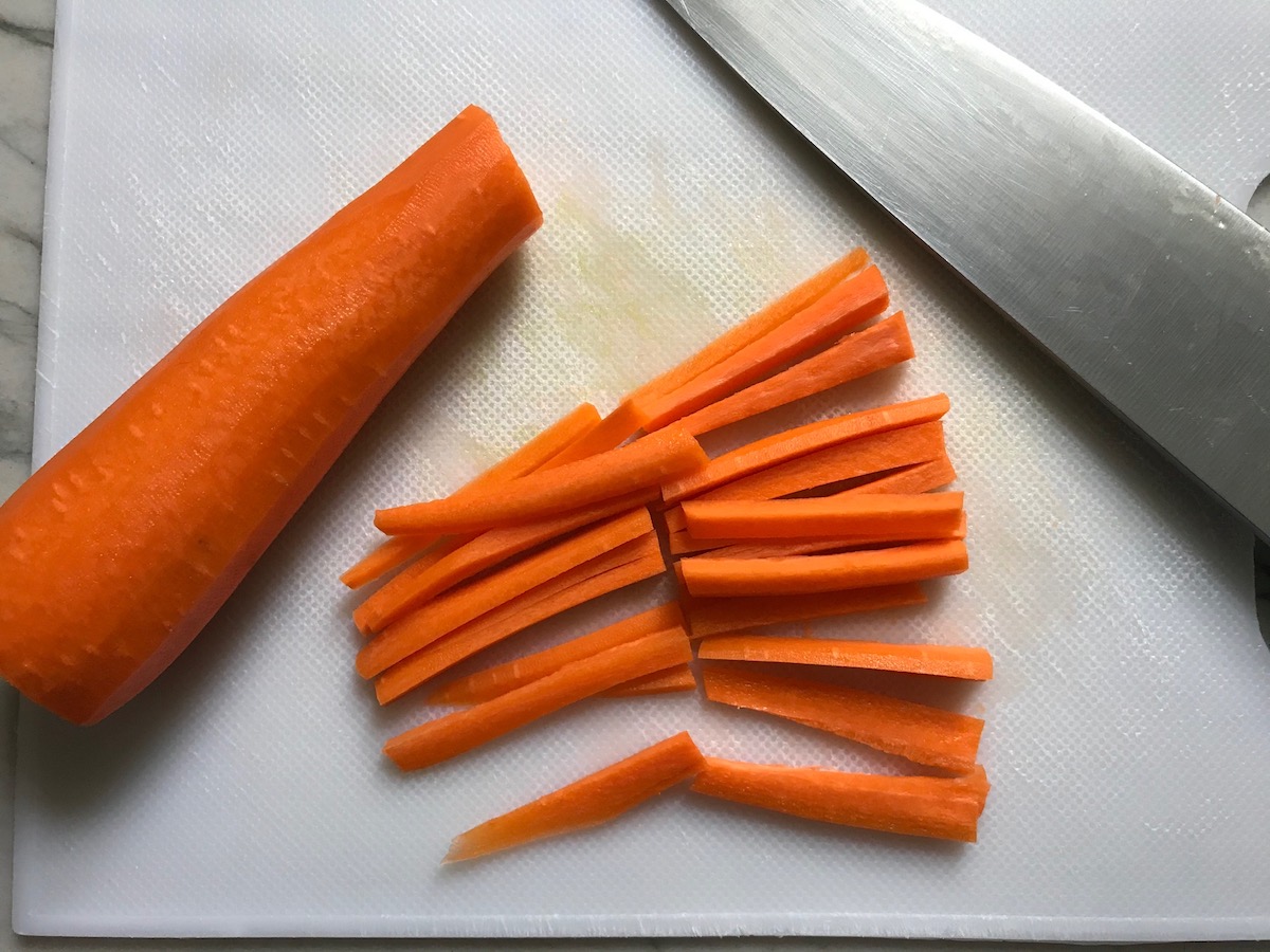 Carrot sticks cut on cutting board with knife for low carb Chicken Lettuce Wraps.