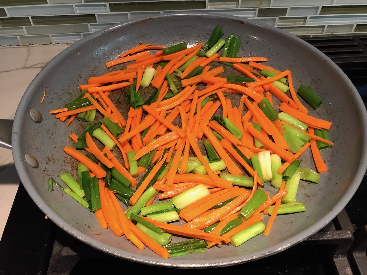 Carrot sticks and scallions cooking in a pan for low carb Chicken Lettuce Wraps.