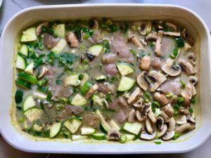 Raw chicken, zucchini, scallions, and mushrooms mixed in casserole dish over rice and broth for Chicken Wild Rice Casserole with Zucchini and Mushrooms.