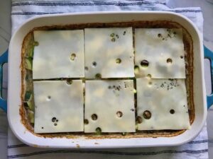 6 slices of swiss cheese added to the top of Chicken Wild Rice Casserole with Zucchini and Mushrooms in a casserole dish