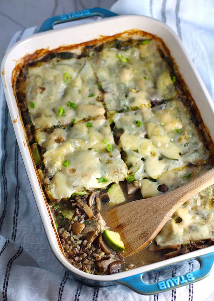 Chicken Wild Rice Casserole with Zucchini and Mushrooms in a casserole dish with missing corner piece and wood spatula in dish.