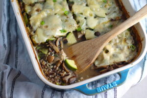 Chicken Wild Rice Casserole with Zucchini and Mushrooms in a casserole dish with missing corner piece and wood spatula in dish.