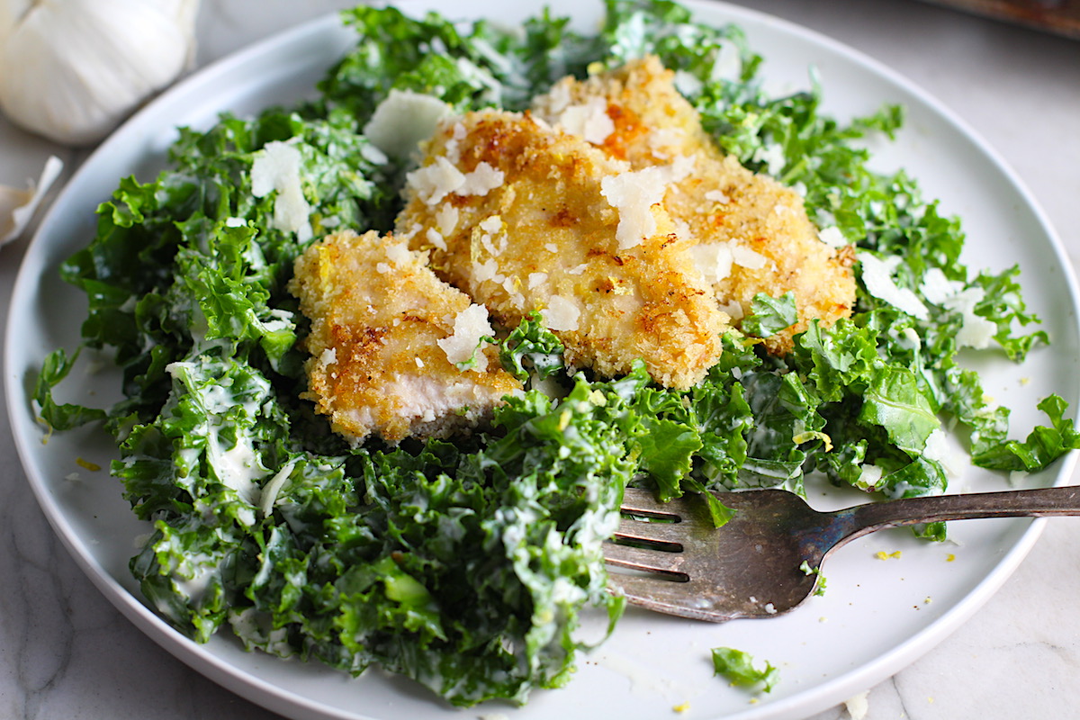 Crispy Lemon Chicken Kale Caesar Salad with chicken strips on top on a plate with a fork.