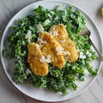 Kale Caesar Salad with Baked Crispy Lemon Chicken strips on top on a plate with a fork.