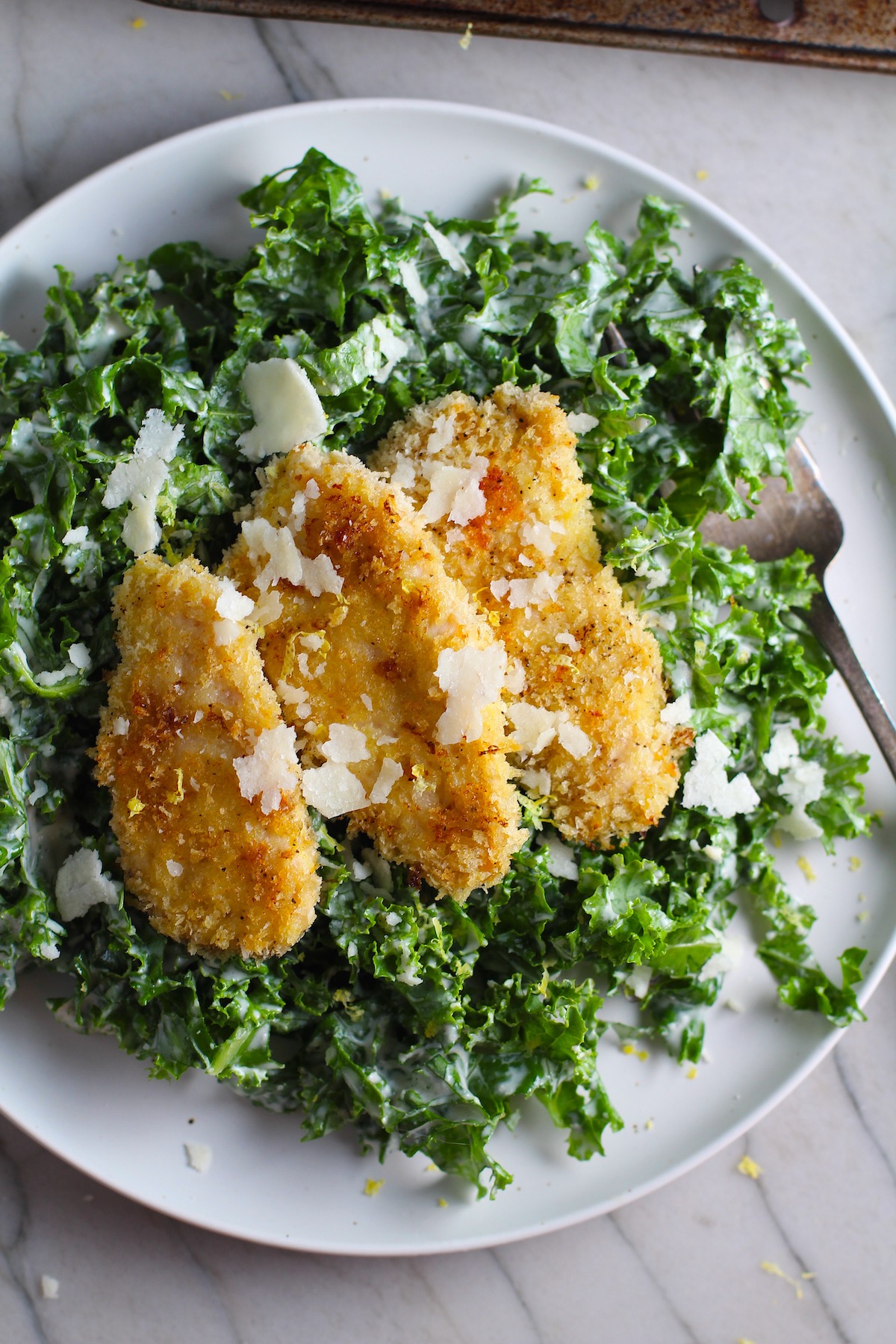 Crispy Lemon Chicken Kale Caesar Salad with chicken strips on top on a plate with a fork.