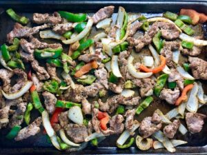 Cooked seasoned strips of pork tenderloin, onion, red pepper, and green pepper on a sheet pan for the Sheet Pan Pork Fajitas Recipe.
