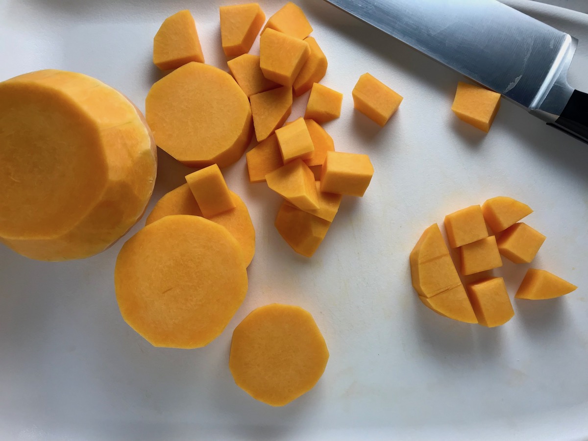 Butternut squash on cutting board, cut into round discs and then cubed for Butternut Squash and Chicken with Shallots.