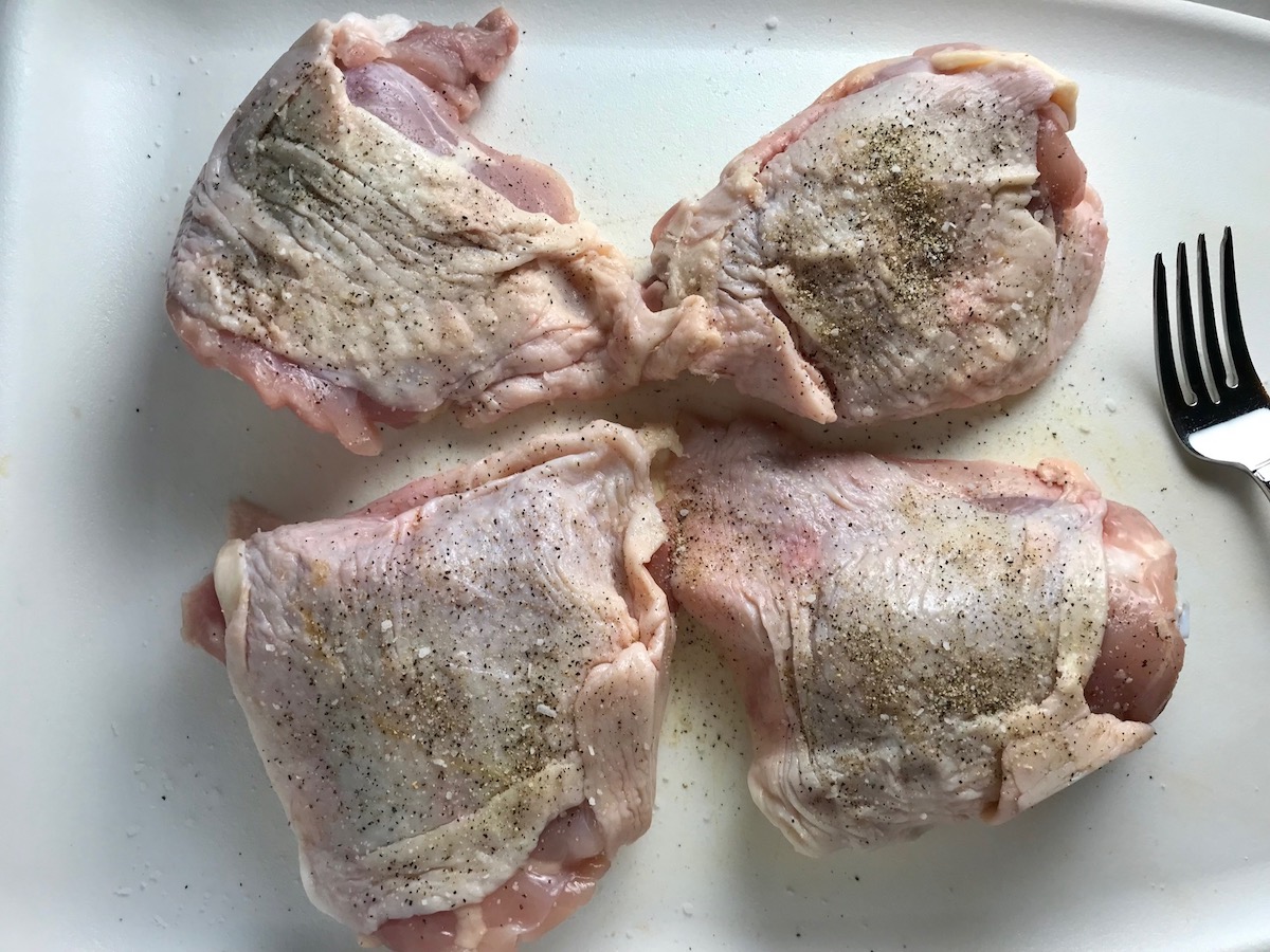 Raw chicken thighs with the skin on and seasoned with salt, pepper, and garlic powder for Butternut Squash and Chicken with Shallots.