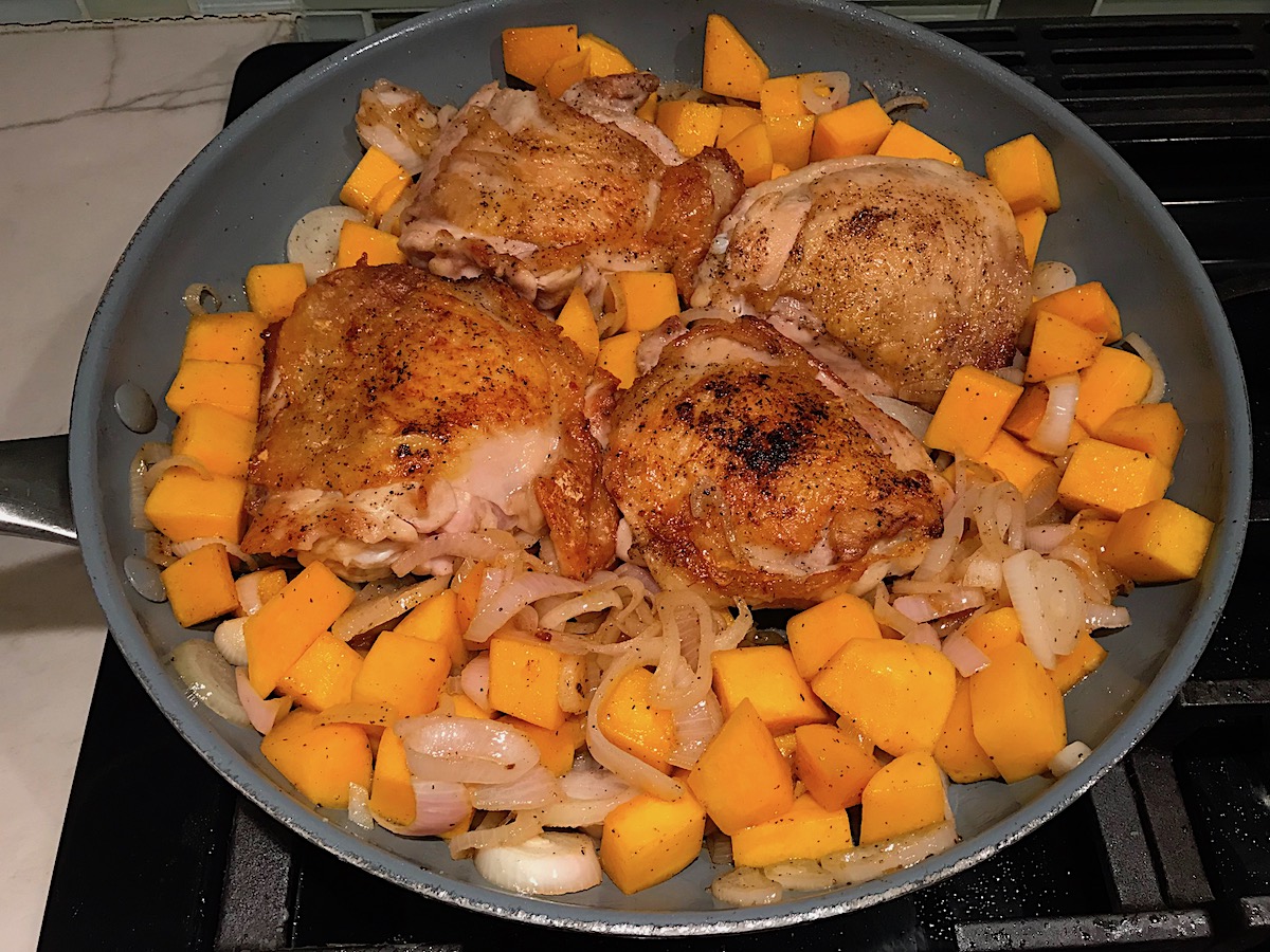 Seared chicken thighs, butternut squash cubes and shallots cooking in a frying pan for Butternut Squash and Chicken with Shallots.