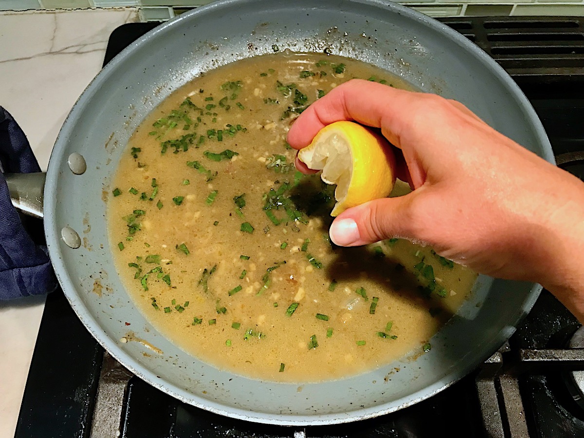 Hand squeezing a lemon over pan with sage and butter for Butternut Squash and Chicken with Shallots.