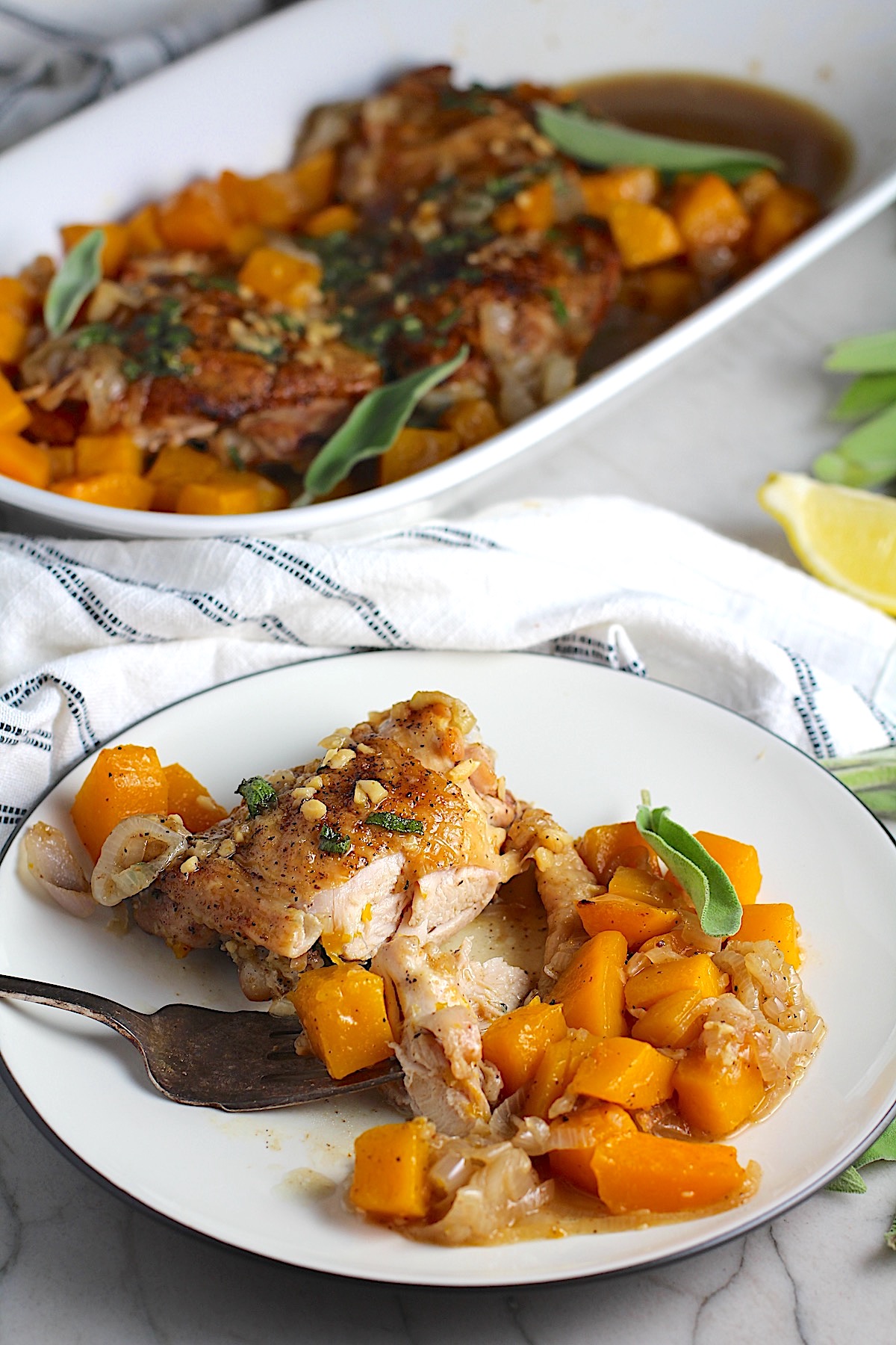 Butternut Squash and Chicken with sage, garlic, and shallots on a plate with fork holding a bite of the chicken and a platter in the background.
