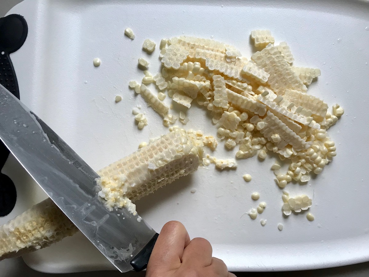 Knife cutting corn kernels off cob for Southwestern Pasta with Ground Beef and Corn and breadcrumbs. The sauce is thick and hearty with ground beef, sweet corn kernels, chunky tomatoes, chipotle peppers in adobo, green chiles, parmesan cheese, and lots of smokey and spicy seasonings.