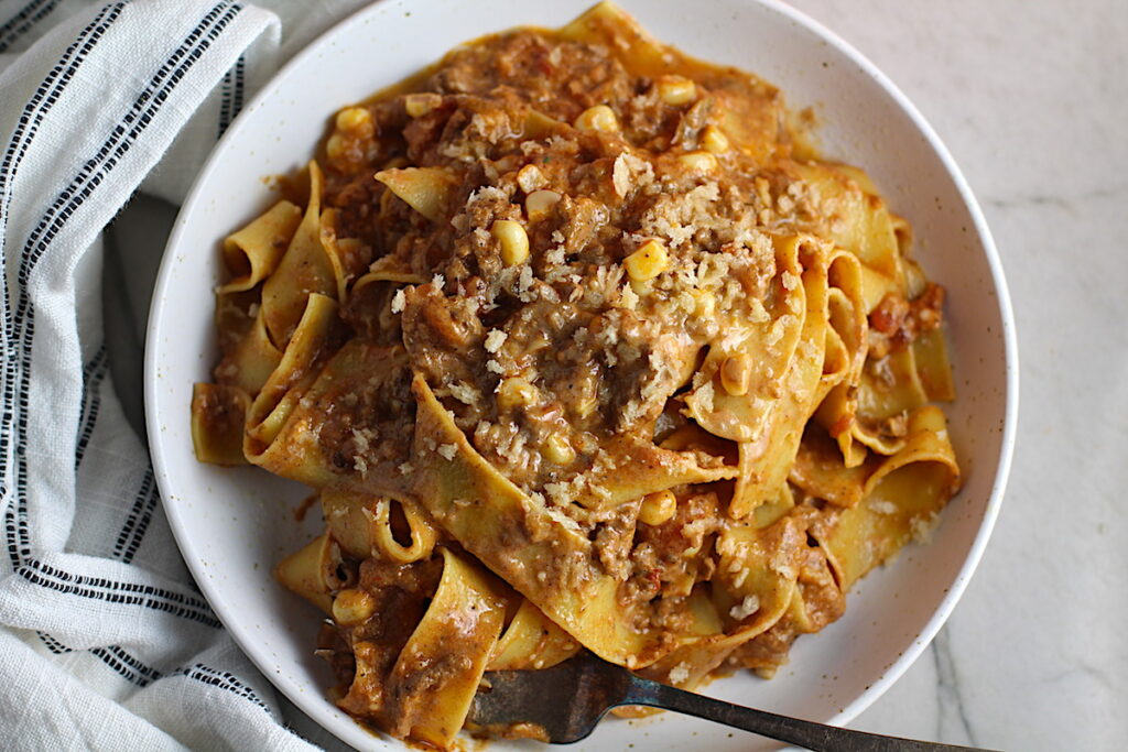 Southwestern Pasta with Ground Beef and Corn and breadcrumbs on top on a plate with fork holding a bite. The sauce is thick and hearty with ground beef, sweet corn kernels, chunky tomatoes, chipotle peppers in adobo, green chiles, parmesan cheese, and lots of smokey and spicy seasonings.