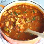 Chicken Goulash with quick homemade dumplings, red pepper, and parsley in a pot with a wood spoon.