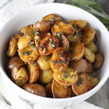 Crispy browned Sage Baby Potatoes with Garlic Butter in a bowl with garlic, sage butter glistening on top.