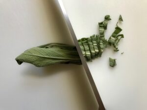 Knife slicing fresh sage leaves for Sage Butter Potatoes.