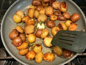 Browned and crispy halved red and gold creamer potatoes in a skillet with garlic, sage, and melted butter for Sage Butter Potatoes.