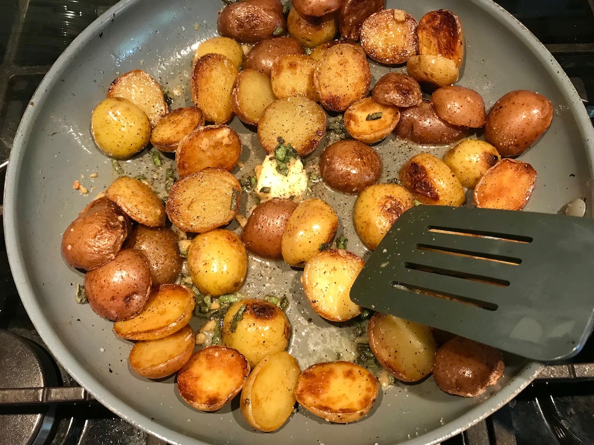 Browned and crispy halved red and gold creamer potatoes in a skillet with garlic, sage, and melted butter for Sage Butter Potatoes.