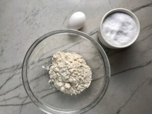 Flour in a bowl on counter with whole egg next to it and salt in bowl for Chicken Goulash with quick homemade dumplings.