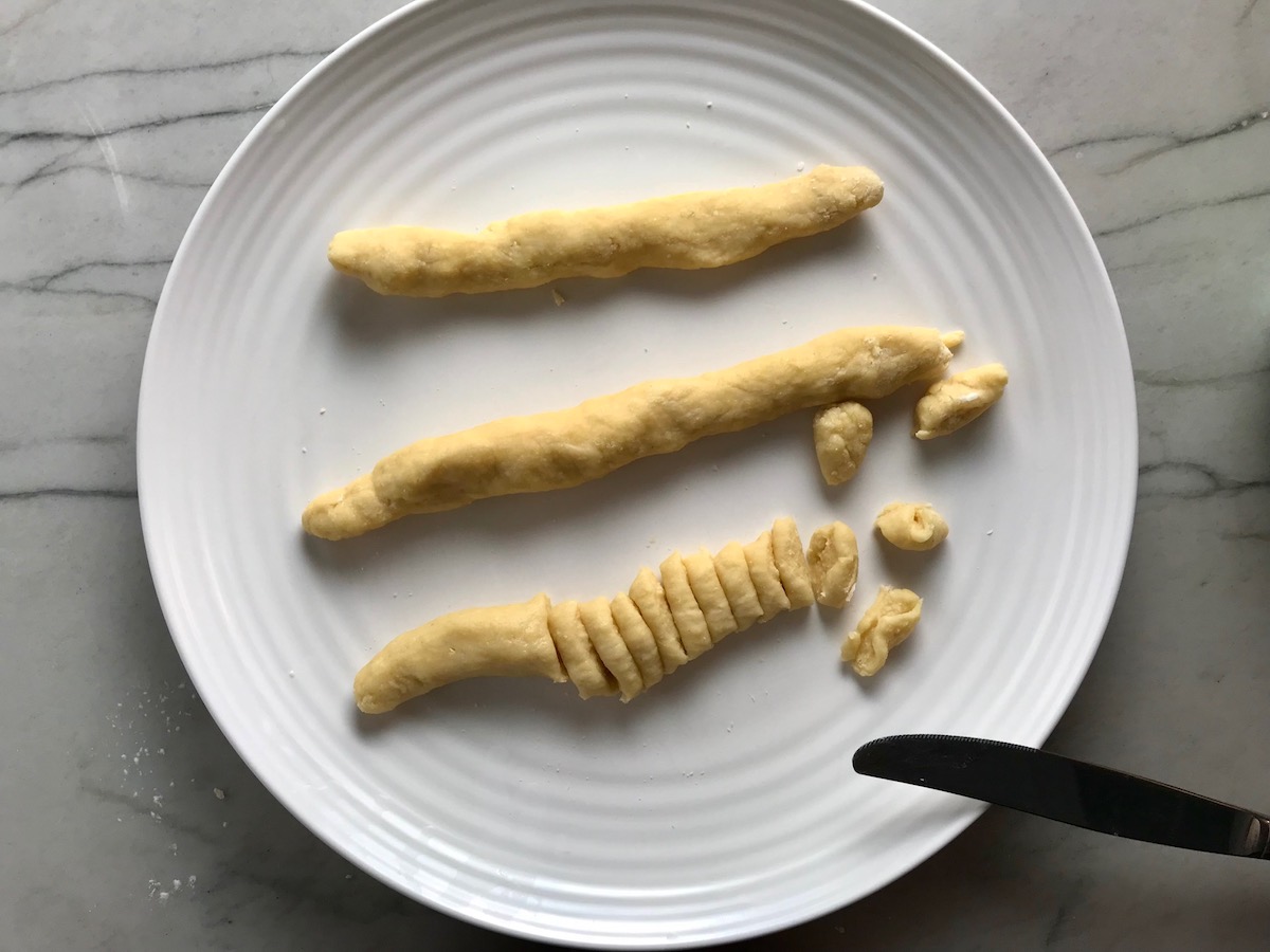 Knife cutting dumplings from 3 slender dough ropes on a plate on counter for Chicken Goulash with quick homemade dumplings.