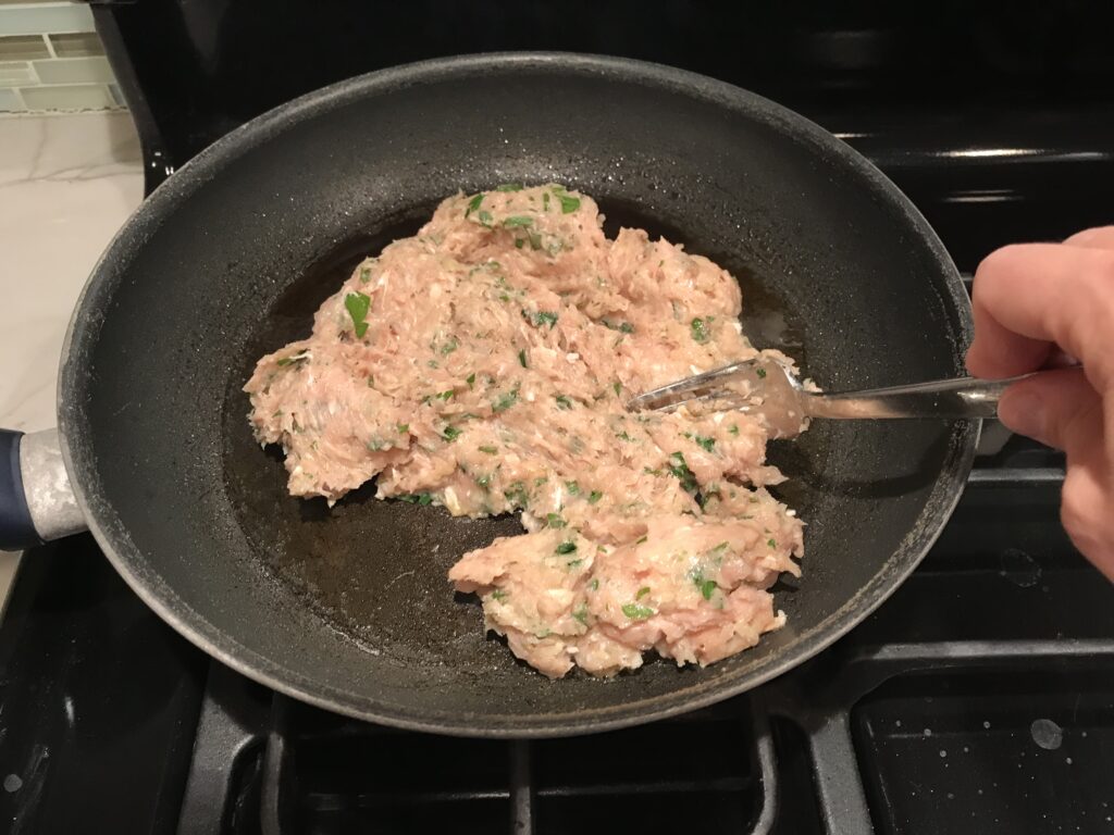 Ground Italian Chicken Sausage in a frying pan with fork breaking it apart into pieces.
