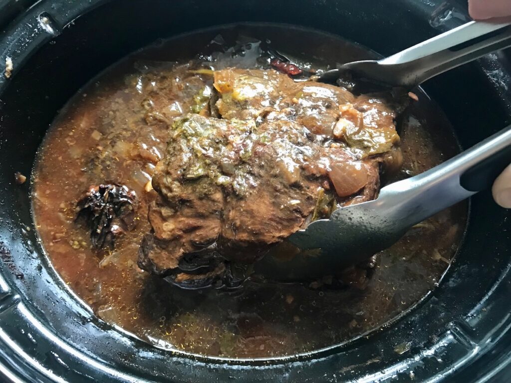 Tongs pulling cooked Beef Chuck Roast from slow cooker for Mexican Shredded Beef.