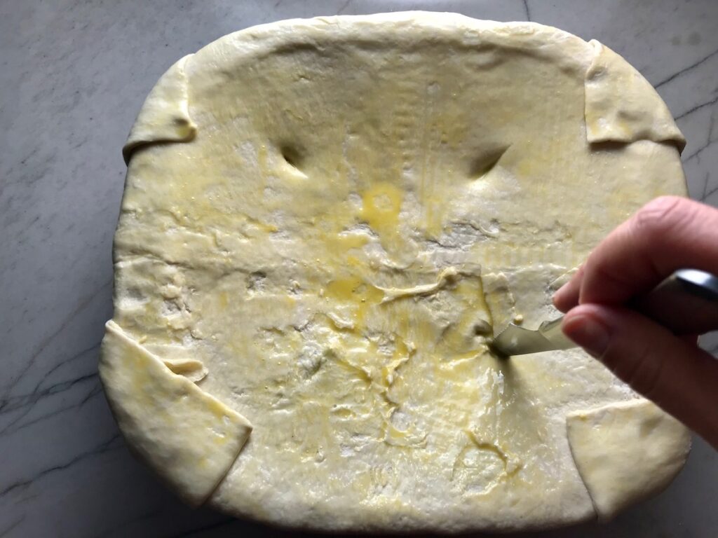 Knife cutting slits into puff pastry dough for Puff Pastry Turkey Pot Pie is an easy dinner recipe to use leftover turkey from the holidays and ingredients you can have on hand! The vegetables and sauce come together so easily and store-bought puff pastry is a time saver.