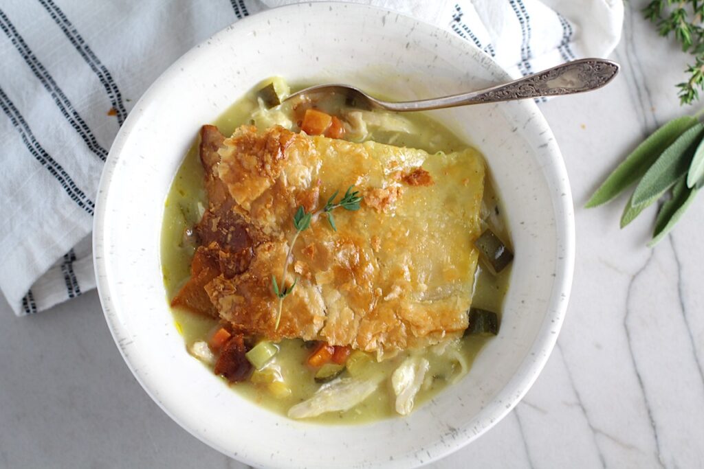 Puff Pastry Turkey Pot Pie serving in a bowl with spoon and fresh thyme and sage on the side. It's an easy dinner recipe to use leftover turkey from the holidays and ingredients you can have on hand!