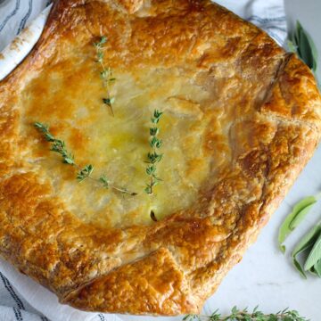 Puff Pastry Turkey Pot Pie in a casserole dish with fresh thyme on top and fresh sage on the counter. It's an easy dinner recipe to use leftover turkey from the holidays and ingredients you can have on hand!