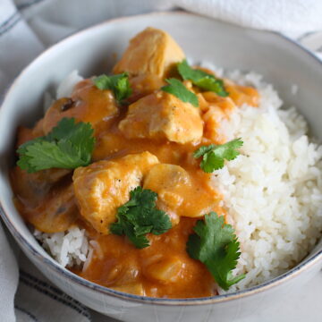 Chicken Stroganoff Brazilian Style in a bowl with a tomato based sauce, cream, mushrooms and cilantro leaves on top all over rice.