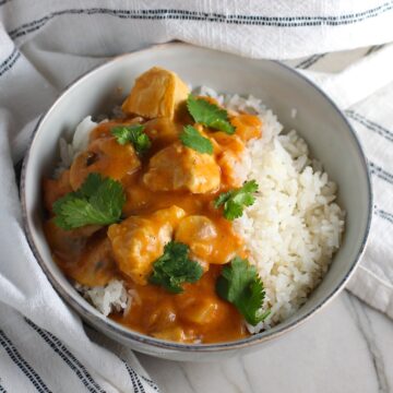 Chicken Stroganoff Brazilian Style in a bowl with a tomato based sauce, cream, mushrooms and cilantro leaves on top all over rice.