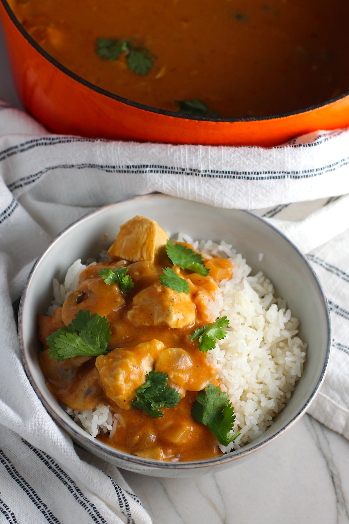 Chicken Stroganoff Brazilian Style in a bowl with a tomato based sauce, cream, mushrooms and cilantro leaves on top all over rice. Pot in background.