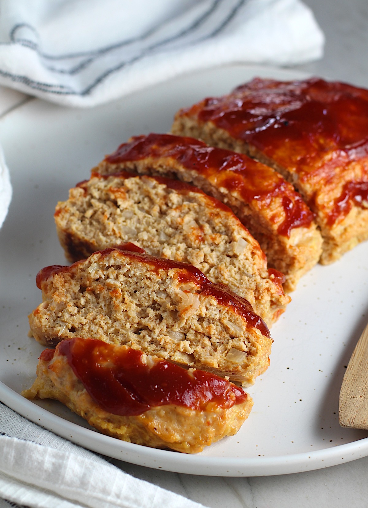 Ground Chicken Meatloaf with ketchup on top sliced and fanned out on plate with spatula on side and towel next plate. It's a perfect family dinner main dish! 10 minutes to prep and 45 minutes to bake.