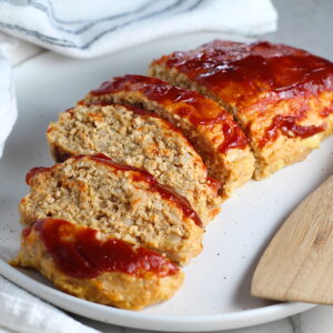 Ground Chicken Meatloaf with ketchup on top sliced and fanned out on plate with spatula on side and towel next plate. It's a perfect family dinner main dish! 10 minutes to prep and 45 minutes to bake.
