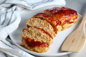 Ground Chicken Meatloaf with ketchup on top sliced and fanned out on plate with spatula on side and towel next plate. It's a perfect family dinner main dish! 10 minutes to prep and 45 minutes to bake.