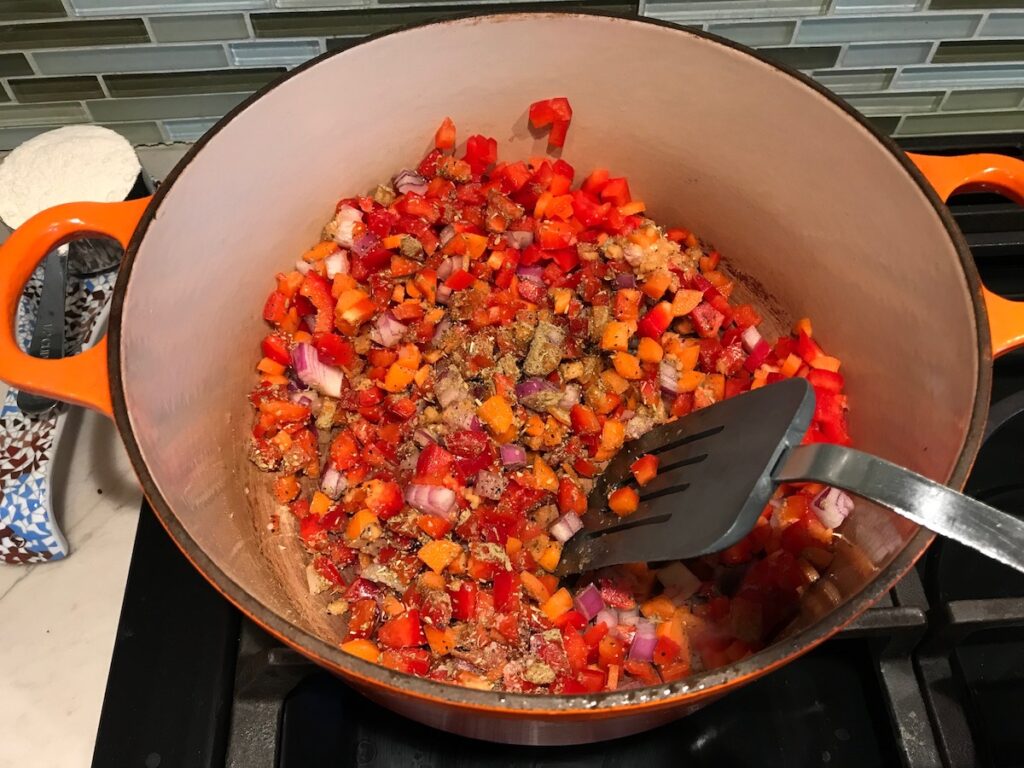 Spatula stirring seasonings into veggies in pot for Red Pepper and Lentil Soup. This is an easy and hearty lunch or dinner! It comes together in just 40 minutes.