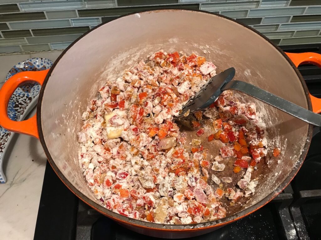Spatula mixing flour into veggies in pot for Red Pepper and Lentil Soup. This is an easy and hearty lunch or dinner! It comes together in just 40 minutes.