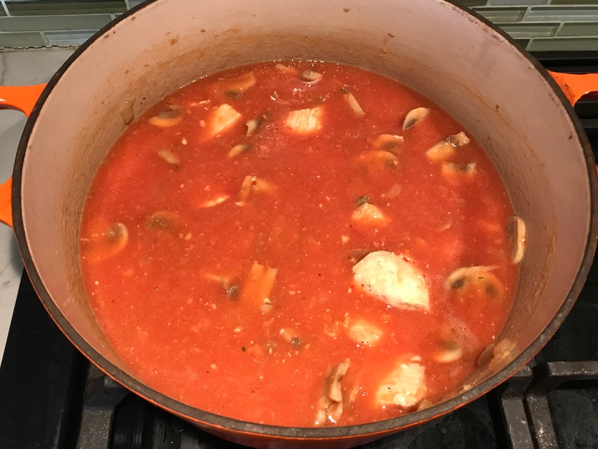 Tomato sauce and broth added to pot with chicken and mushrooms on stove for Chicken Stroganoff Brazilian Style. It's an easy 30 minute dinner with a tomato based sauce, cream, and mushrooms all over rice.