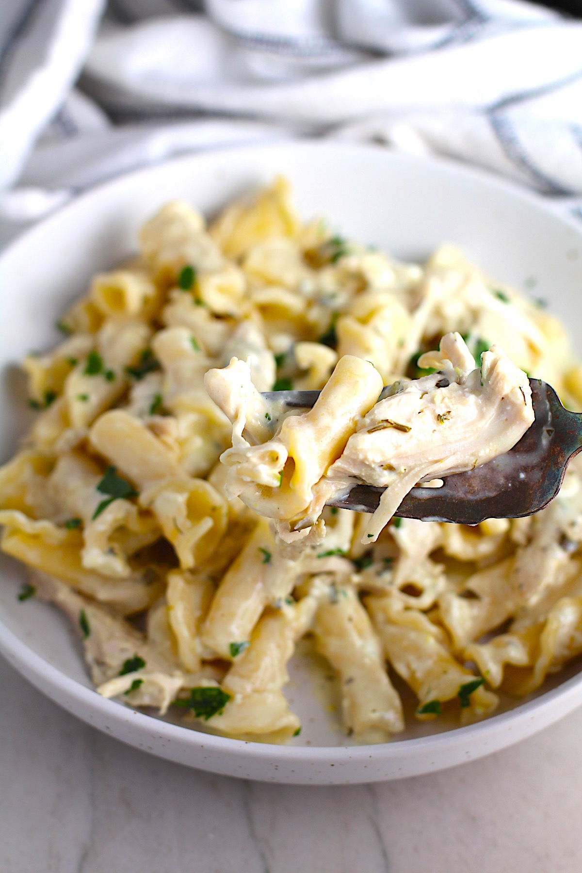 Ranch Chicken Crock Pot Pasta on a plate with fork and towel next it on counter. It uses fresh dill, parsley, and scallions is creamy, tangy, and utterly delicious! It's also so easy to make, so it's a great weeknight dinner.
