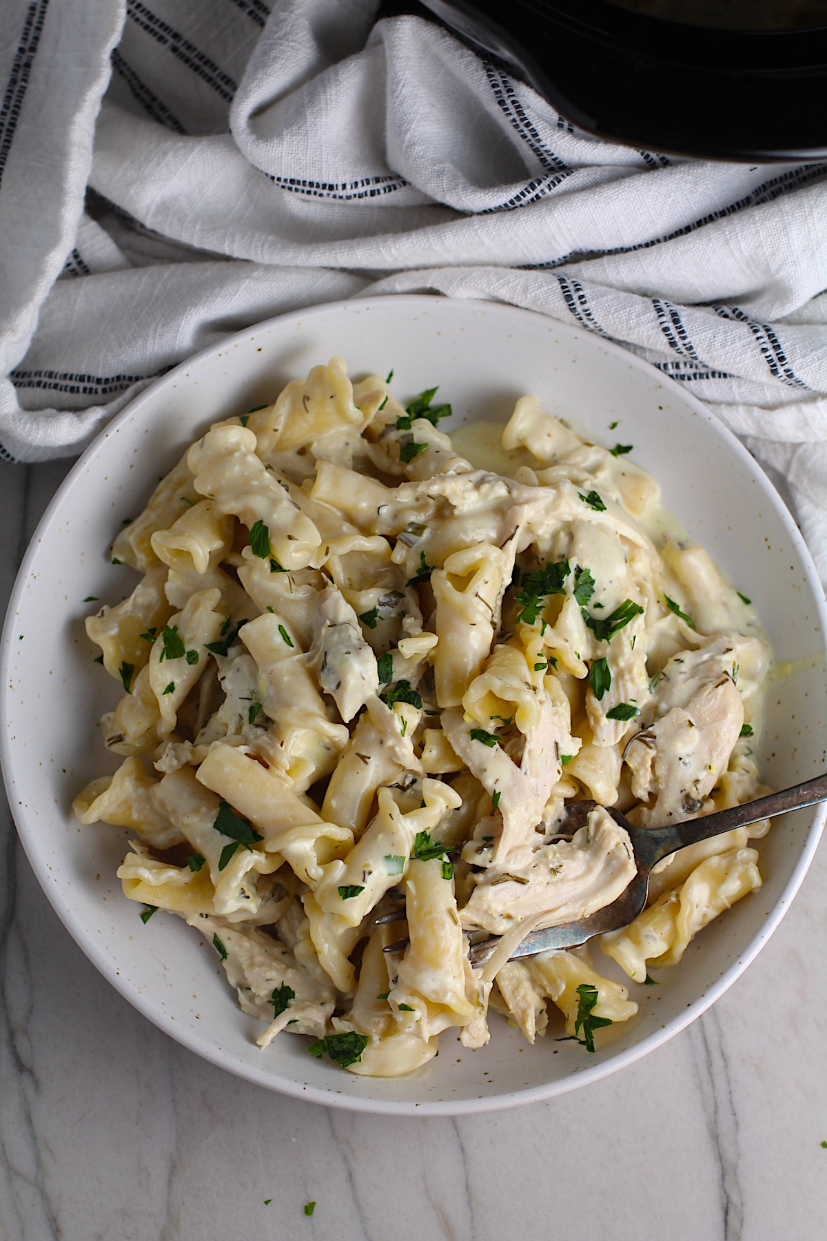 Ranch Chicken Crock Pot Pasta on a plate with fork and towel next it on counter. It uses fresh dill, parsley, and scallions is creamy, tangy, and utterly delicious! It's also so easy to make, so it's a great weeknight dinner.