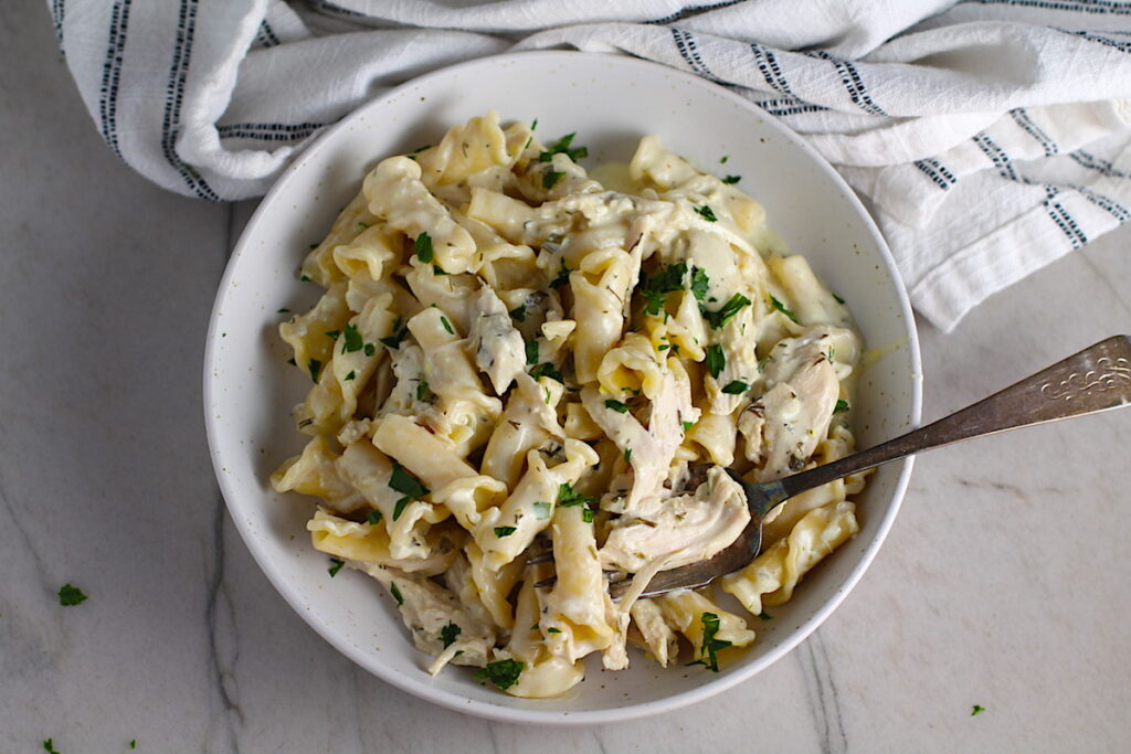 Ranch Chicken Crock Pot Pasta on a plate with fork and towel next it on counter. It uses fresh dill, parsley, and scallions is creamy, tangy, and utterly delicious! It's also so easy to make, so it's a great weeknight dinner.