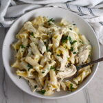 Ranch Chicken Crock Pot Pasta on a plate with fork and towel next it on counter. It uses fresh dill, parsley, and scallions is creamy, tangy, and utterly delicious!  It's also so easy to make, so it's a great weeknight dinner.