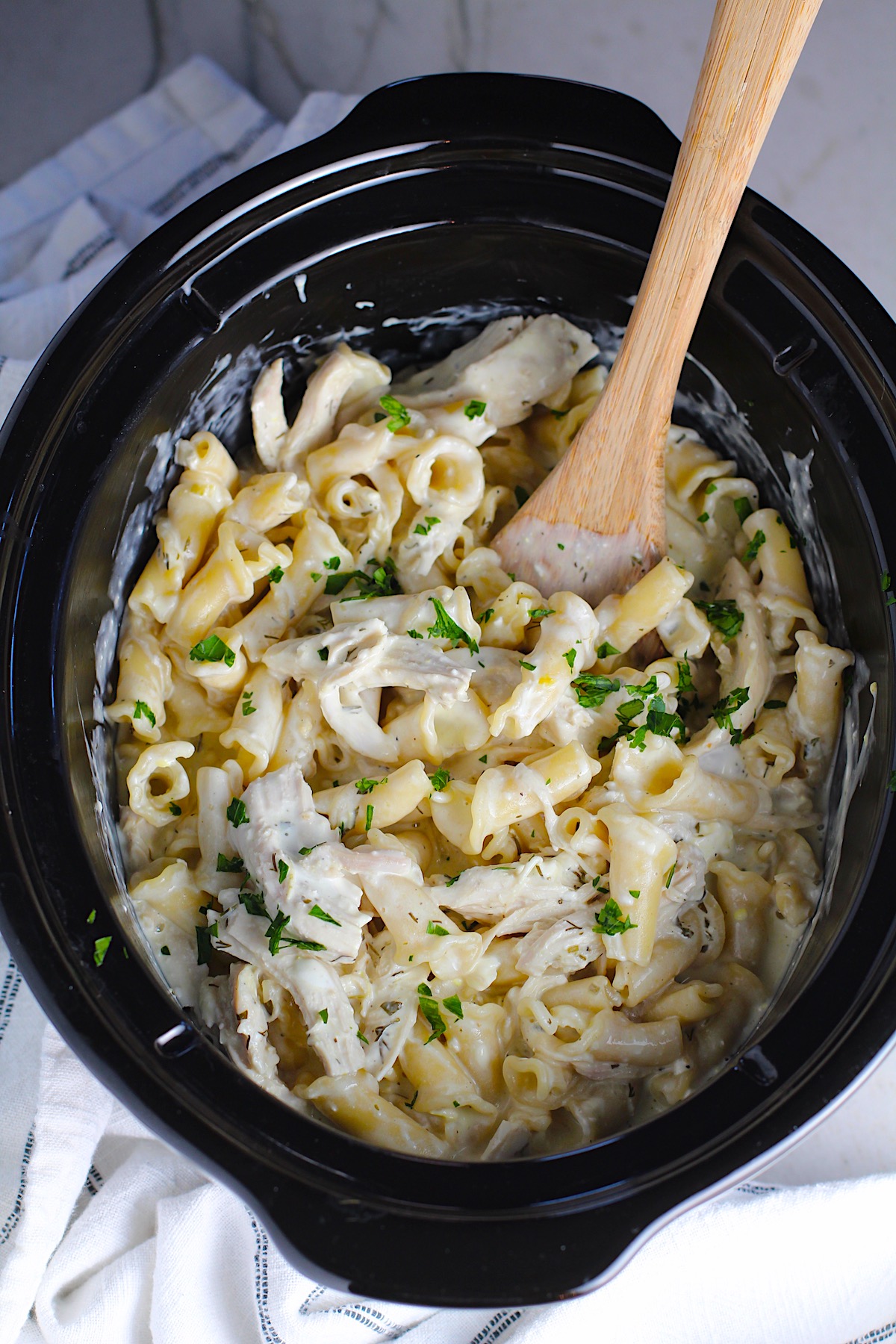 Ranch Chicken Crock Pot Pasta in the crockpot with wood spoon using fresh dill, parsley, and scallions is creamy, tangy, and utterly delicious! It's also so easy to make, so it's a great weeknight dinner.