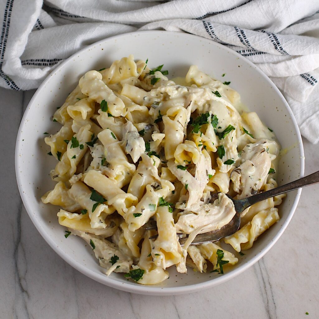 Ranch Chicken Crock Pot Pasta on a plate with fork and towel next it on counter. It uses fresh dill, parsley, and scallions is creamy, tangy, and utterly delicious! It's also so easy to make, so it's a great weeknight dinner.