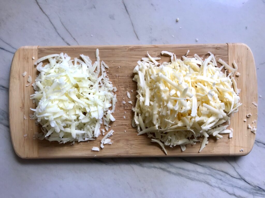 Two piles of shredded cheese on a wood cutting board on counter for freezer idea post 'Can you freeze pulled pork'.
